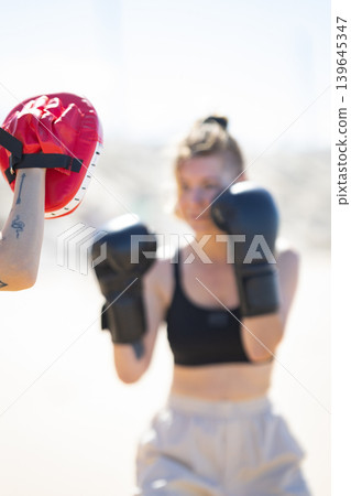 Woman training boxing striking focus mitt outdoors Woman training boxing striking focus mitt outdoors 139645347