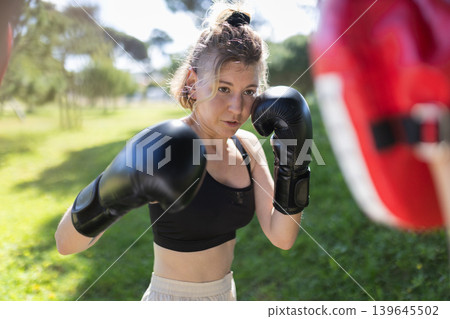 Woman training boxing striking focus mitts outdoors Woman training boxing striking focus mitts outdoors 139645502