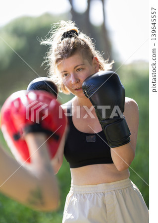 Woman training boxing with punch mitts outdoors Woman training boxing with punch mitts outdoors 139645557