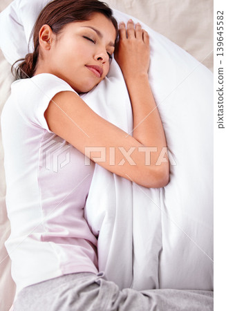 Sleeping, pillow and woman relax in bedroom for comfort, cozy nap and rest with eyes closed in home apartment. Top view, fatigue and Mexican person sleep on mattress bed with calm, peace and wellness 139645582