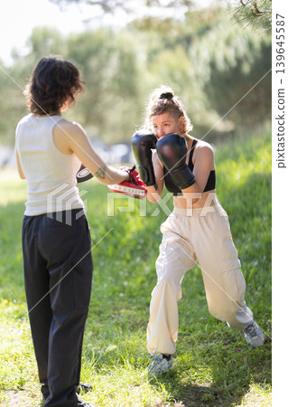 Women training boxing outdoors with punch mitts Women training boxing outdoors with punch mitts 139645587