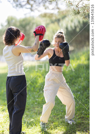 Women training boxing outdoors practicing punches with mitts Women training boxing outdoors practicing punches with mitts 139645616