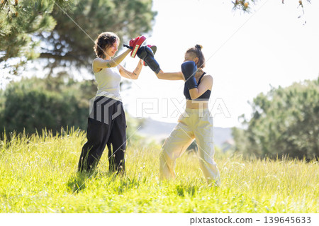 Women training boxing outdoors holding focus mitts Women training boxing outdoors holding focus mitts 139645633