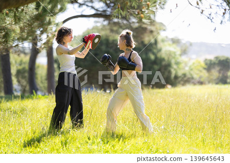 Two women training boxing punches outdoors in grass Two women training boxing punches outdoors in grass 139645643