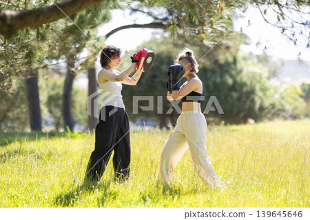 Women training boxing with focus mitts outdoors for fitness Women training boxing with focus mitts outdoors for fitness 139645646