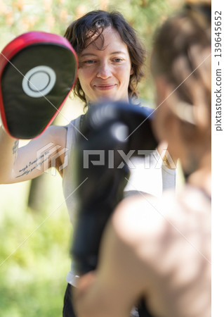Woman holding boxing pad during outdoor training Woman holding boxing pad during outdoor training 139645652