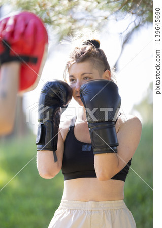 Woman training boxing hitting focus mitt outdoors 139645690