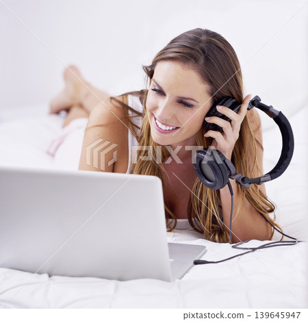 Morning, woman in bed with laptop and headphones to relax with streaming service for podcast, radio or audio. Bedroom, smile and girl with computer, earphones and listening to music with online app. 139645947