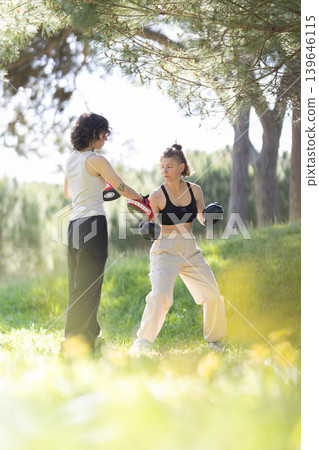 Women training boxing hitting punch mitts outdoors Women training boxing hitting punch mitts outdoors 139646115