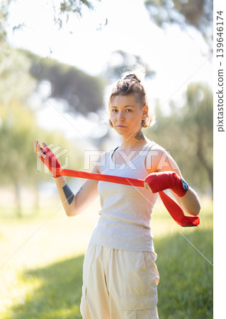 Determined young woman wrapping red boxing hand wraps Determined young woman wrapping red boxing hand wraps 139646174