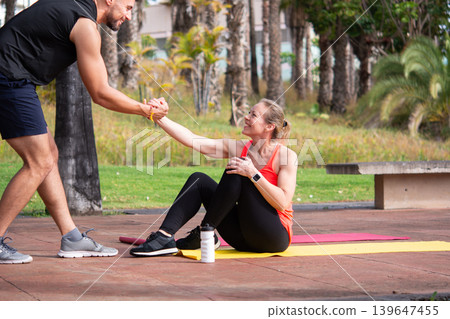 Personal trainer helping mature woman during outdoor fitness workout in park Personal trainer helping mature woman during outdoor fitness workout in park 139647455
