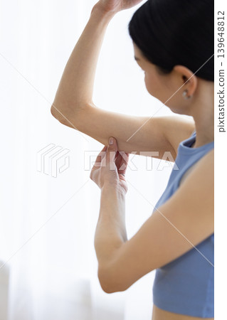 Japanese woman in yoga wear pinching her upper arm Japanese woman in yoga wear pinching her upper arm 139648812