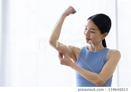 Japanese woman in yoga wear pinching her upper arm Japanese woman in yoga wear pinching her upper arm 139648813