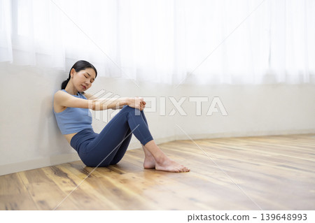 一名身穿瑜珈服的日本女子麵露疲憊之色，坐在地板上。 139648993