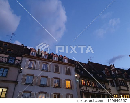 Phone photo of traditional half-timbered houses in Alsace at twilight. Charming European architecture scene with timber frames, pastel facades, and soft blue hour light. Phone photo of traditional half-timbered houses in Alsace at twilight. Charming European architecture scene with timber frames, pastel facades, and soft blue hour light. 139649267