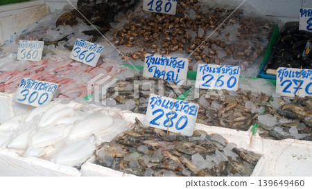 Fresh seafood displayed at outdoor market counter with Thai language price signs reading shrimp, squid and mollusks. Local Asian market concept Fresh seafood displayed at outdoor market counter with Thai language price signs reading shrimp, squid and mollusks. Local Asian market concept 139649460