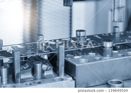 Industrial operation of a progressive die forming high-precision sheet metal parts in a blue-toned scene with lighting effects. 139649504