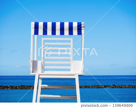 White lifeguard tower with blue striped canopy overlooking calm ocean under clear sky. Minimal tropical beach scene with copy space and summer travel mood White lifeguard tower with blue striped canopy overlooking calm ocean under clear sky. Minimal tropical beach scene with copy space and summer travel mood 139649800