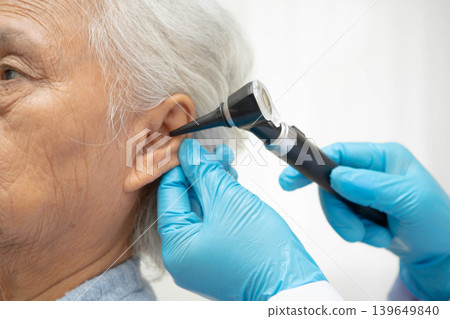 Otolaryngologist or ENT physician doctor examining senior patient ear with otoscope, hearing loss problem. Otolaryngologist or ENT physician doctor examining senior patient ear with otoscope, hearing loss problem. 139649840