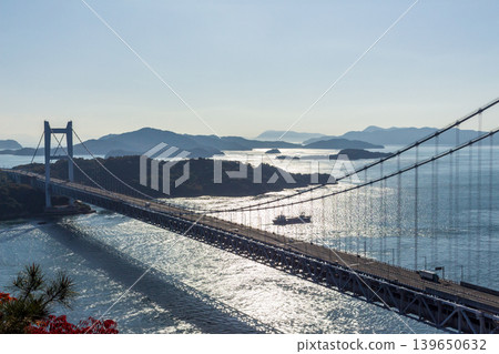 Cars crossing the Seto Ohashi Bridge (Shimotsui Seto Ohashi Bridge) and cargo ships sailing against the backdrop of the Seto Inland Sea, which is illuminated by the sun. Cars crossing the Seto Ohashi Bridge (Shimotsui Seto Ohashi Bridge) and cargo ships sailing against the backdrop of the Seto Inland Sea, which is illuminated by the sun. 139650632