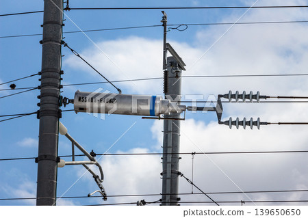 An automatic overhead line tension adjustment device (tension balancer) near Kaga Onsen Station on the Hokuriku Shinkansen line, against a blue sky. 139650650