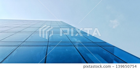 Low angle of blue glass facade of a modern, symmetrical office building Low angle of blue glass facade of a modern, symmetrical office building 139650754