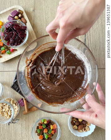 a person's hands actively whisking a thick, glossy dark chocolate batter in a clear glass mixing bowl. a person's hands actively whisking a thick, glossy dark chocolate batter in a clear glass mixing bowl. 139651387