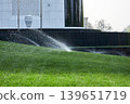 Automatic garden sprinkler watering green grass lawn. System spraying water on backyard landscaping. Ecological maintenance of public park and professional irrigation technology concept. 139651719