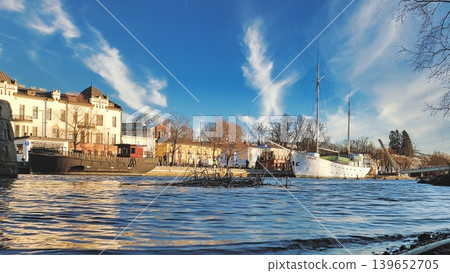 Porvoo, Finland - December 08, 2020: Scenic waterfront view features boats docked along the shore, with a vibrant blue sky and wispy clouds creating a picturesque atmosphere Porvoo, Finland - December 08, 2020: Scenic waterfront view features boats docked along the shore, with a vibrant blue sky and wispy clouds creating a picturesque atmosphere 139652705