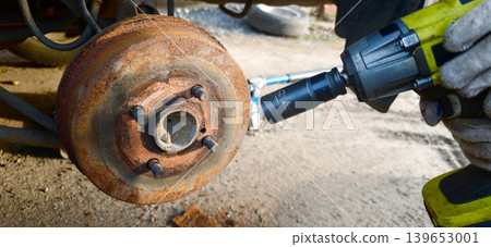Car mechanic repairs brake disc and drum with power tools on vehicle Car mechanic repairs brake disc and drum with power tools on vehicle 139653001