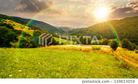 sunset over rural field on the hill. view in to the valley. countryside mountain landscape. alpine pasture near forested hills. timeless nostalgia book cover with rainbow sunset over rural field on the hill. view in to the valley. countryside mountain landscape. alpine pasture near forested hills. timeless nostalgia book cover with rainbow 139653059