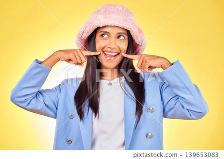 Fashion, smile and face of Indian woman on yellow background with silly, goofy and playful expression. Emoji, happiness and person in studio pointing to mouth in trendy accessories, style and hat 139653083