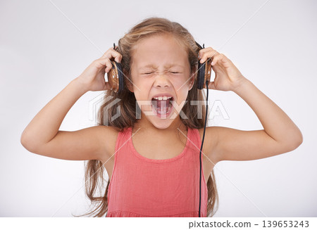 Child, headphones and screaming in studio for music entertainment, rock or streaming. Female person, girl and shout for listening audio or radio noise or loud sing, white background or mockup space Child, headphones and screaming in studio for music entertainment, rock or streaming. Female person, girl and shout for listening audio or radio noise or loud sing, white background or mockup space 139653243