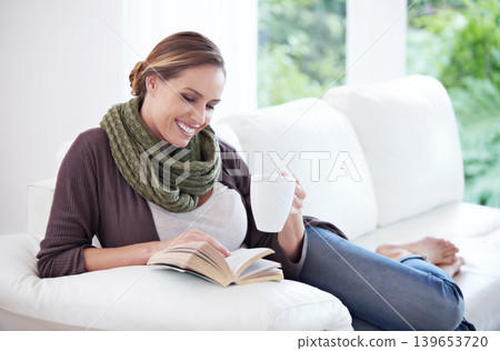 Happy, woman and reading book with coffee on sofa for story, novel or hobby in living room at home. Lady, fiction books and drinking cup of tea for literature, knowledge or comfortable break on couch 139653720
