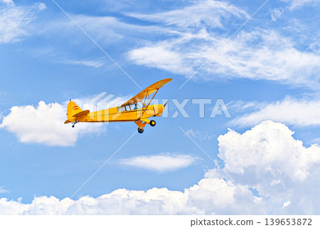 A yellow single-engine ultralight aircraft flying in a blue sky with white clouds. A yellow single-engine ultralight aircraft flying in a blue sky with white clouds. 139653872