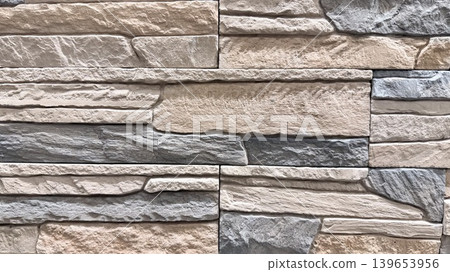 Beige and gray stone wall texture in close-up with layered decorative masonry pattern. 139653956