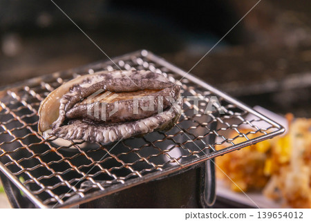 Abalone in its shell, placed on a charcoal grill; fresh abalone before grilling. Abalone in its shell, placed on a charcoal grill; fresh abalone before grilling. 139654012