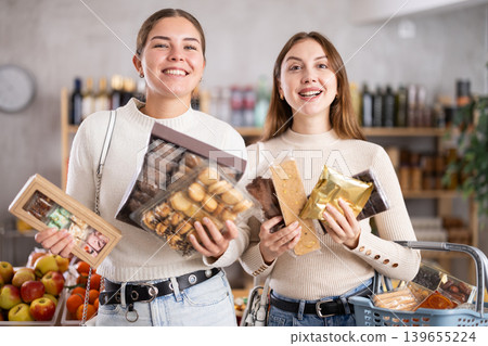 Two friends buy various sweets together - cookies and nougat in grocery supermarket Two friends buy various sweets together - cookies and nougat in grocery supermarket 139655224