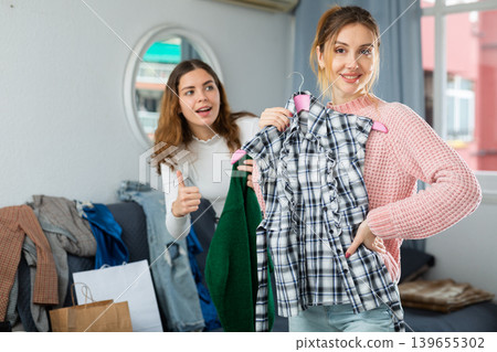 Portrait of two women showing each other and trying clothes in home Portrait of two women showing each other and trying clothes in home 139655302