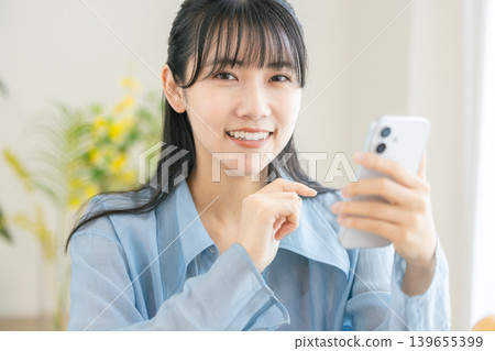 一位年輕女子早上正在用智慧型手機梳妝打扮。 一位年輕女子早上正在用智慧型手機梳妝打扮。 139655399
