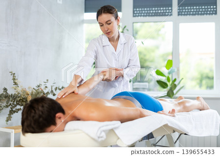 During massage, female physiotherapist stretche man client arm to improve mobility of shoulder joint 139655433