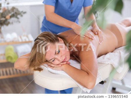 Woman relaxing while professional masseuse doing back massage Woman relaxing while professional masseuse doing back massage 139655540