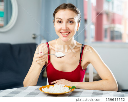 Young woman eating rice while sitting at the table in room. Diet and weight loss concept 139655552