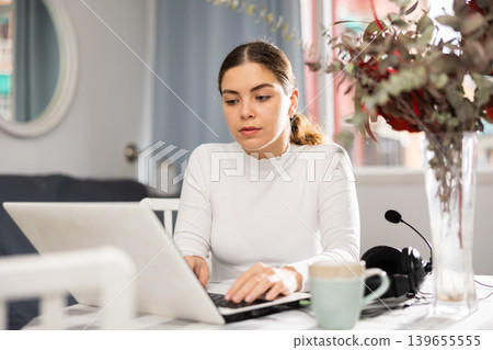 Young woman sitting at table and using laptop Young woman sitting at table and using laptop 139655555