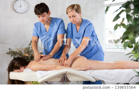 Back massage in four hands simultaneously - two professional masseurs treating woman 139655564