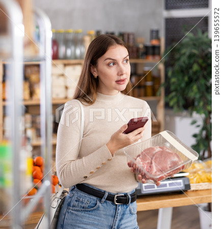 Girl scan QR-code on raw pork package in store 139655572