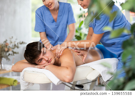 Relaxed guy experiencing back massage performed by two masseuses 139655588