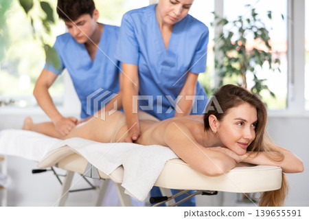 Two unrecognizable female and male masseuses perform stroking and rubbing of muscle of back to girl 139655591