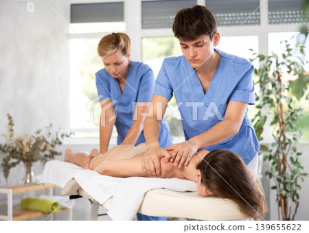 Back massage in four hands simultaneously - two professional masseurs treating woman Back massage in four hands simultaneously - two professional masseurs treating woman 139655622