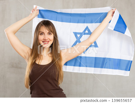 Smiling woman waving flag of Israel against gray background Smiling woman waving flag of Israel against gray background 139655657